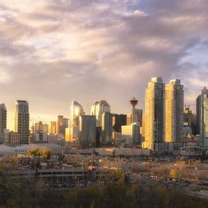 A cityscape with modern skyscrapers and a large domed stadium bathed in the golden light of sunset under a cloudy sky.