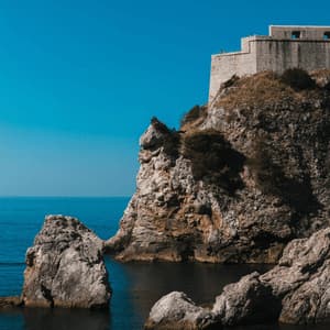 Eine Steinfestung thront auf einer felsigen Klippe mit Blick auf ein tiefblaues Meer unter einem klaren Himmel.