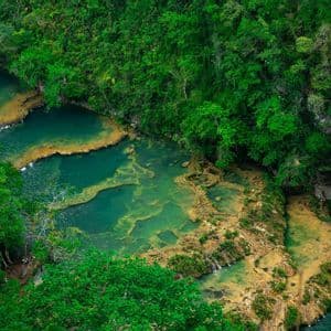 Vue plongeante sur des piscines turquoise en terrasses formant une rivière qui traverse une jungle verte dense.