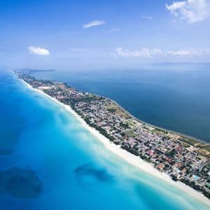 Vue aérienne d'une longue presqu'île présentant une plage de sable blanc, une ville côtière et des eaux contrastées turquoise et bleu profond.