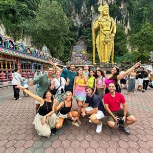 Un gruppo WeRoad posa per una foto davanti a una statua dorata gigante e un tempio colorato alla base di una scogliera boscosa.