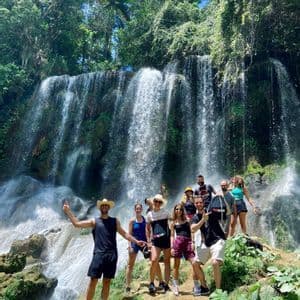 Eine WeRoad-Gruppe posiert für ein Foto auf einem Felsvorsprung vor einem großen, kaskadierenden Wasserfall in einem üppigen Wald.