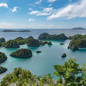 Una vista aérea de numerosas islas verdes y rocosas, dispersas en un mar turquesa bajo un cielo parcialmente nublado.