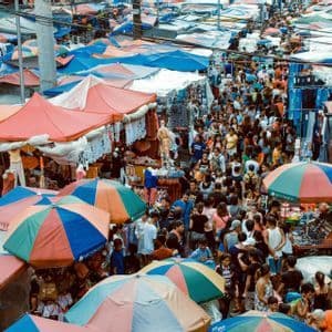 Una vista aérea de un bullicioso mercado callejero al aire libre abarrotado de gente, sombrillas coloridas y puestos de vendedores.