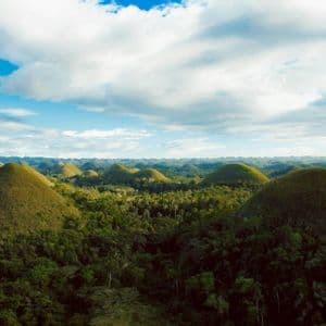 Una vista aérea de numerosas colinas verdes en forma de cono que se elevan desde un bosque exuberante bajo un cielo parcialmente nublado.