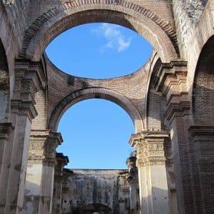 El interior de una ruina de ladrillo sin techo, con grandes arcos y pilares que enmarcan un cielo azul claro.