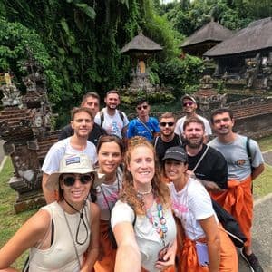 Un groupe WeRoad prend un selfie devant un temple en pierre orné entouré d'une végétation luxuriante.