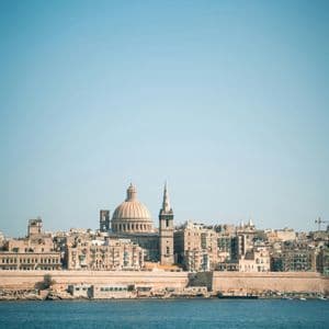Une ville côtière avec un dôme et une flèche proéminents vus depuis l'eau bleue sous un ciel clair.
