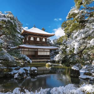 Ein traditioneller japanischer Tempel steht an einem Teich, umgeben von schneebedeckten Bäumen unter klarem blauem Himmel.