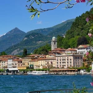 Edificios coloridos de un pueblo bordean la orilla de un lago azul al pie de grandes montañas verdes.