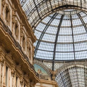 Una fachada de edificio ornamentada con estatuas clásicas se alza junto a un gran techo de cúpula de vidrio y hierro abovedado.