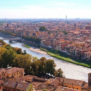 Una vista aérea de una ciudad con un río serpenteante, puentes y edificios de tejados rojos bajo un cielo azul claro.