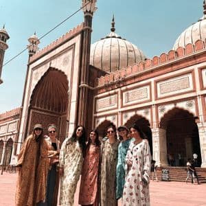Un viaje en grupo de WeRoad de siete mujeres posando en un patio frente a una gran mezquita de arenisca roja con cúpulas blancas.
