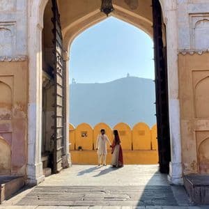 Un couple en tenue indienne traditionnelle se tient sous une grande arche, avec une colline lointaine visible à travers l'ouverture.