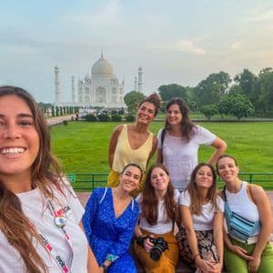 Eine WeRoad Gruppenreise lächelnder Frauen macht ein gemeinsames Selfie vor dem Taj Mahal.