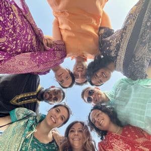 Un groupe WeRoad en voyage, portant des vêtements traditionnels colorés, se rassemble en cercle, souriant à l'appareil photo sous un ciel clair.