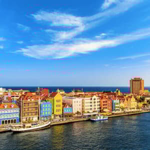 Un paesaggio urbano di edifici colorati lungo un lungomare, con barche ormeggiate nel porto e l'oceano sullo sfondo.