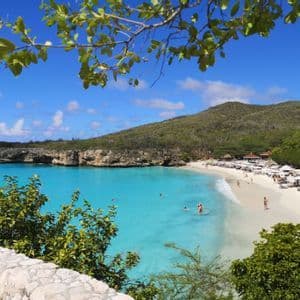 Una vista mozzafiato di una caletta tropicale con persone che nuotano in acqua turchese e si rilassano su una spiaggia di sabbia bianca.