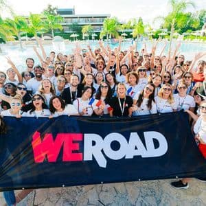 Un grande gruppo WeRoad in viaggio che posa ed esulta per una foto con uno striscione davanti a una piscina.