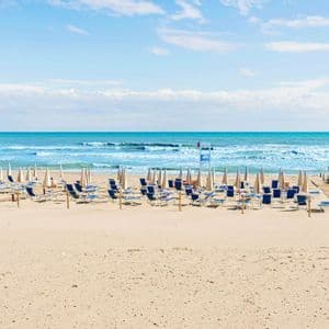 File di sdraio vuote e ombrelloni chiusi sono disposte su una spiaggia sabbiosa con passerelle in legno che conducono verso l'oceano turchese.