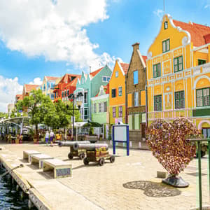 Una passeggiata sul lungomare con edifici colorati, cannoni e una scultura a forma di cuore sotto un cielo blu.