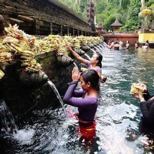 Des personnes effectuent un rituel de purification dans un bassin sacré, priant et déposant des offrandes sous des jets d'eau en pierre.
