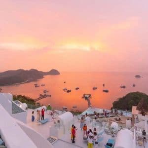Un groupe WeRoad observe le coucher de soleil depuis une terrasse de toit blanche, surplombant une baie avec des bateaux et des îles.