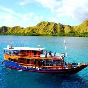 Un voyage de groupe WeRoad sur un bateau en bois à deux ponts dans des eaux calmes et turquoise, avec des îles vertes et vallonnées en arrière-plan.