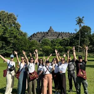 Un voyage de groupe WeRoad posant les mains levées dans un champ herbeux, avec un ancien temple en pierre visible en arrière-plan.