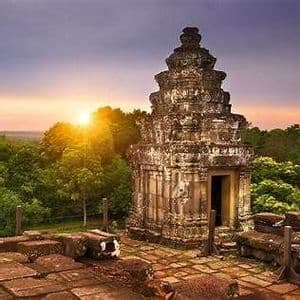 Ein alter, mehrstufiger Steintempel überblickt einen dichten Wald, während die Sonne am Horizont untergeht und ein goldenes Glühen wirft.