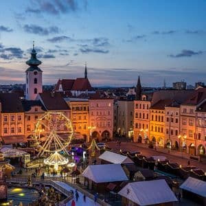 Ein beleuchteter Weihnachtsmarkt erfüllt einen historischen Stadtplatz mit einem Riesenrad, Marktständen und einer Eisbahn bei Einbruch der Dämmerung.
