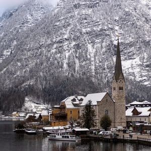 Ein Seeuferdorf mit einer Kirche und einem hohen Kirchturm liegt am Fuße eines großen, schneebedeckten Berges.
