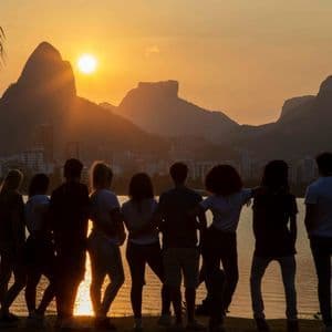 Un viaje en grupo de WeRoad se recorta en la orilla de un lago, viendo el atardecer sobre montañas y una ciudad.