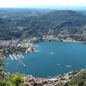 Una vista aerea di una città costiera con un porto turistico, incastonata tra un grande lago blu e rigogliose colline verdi.