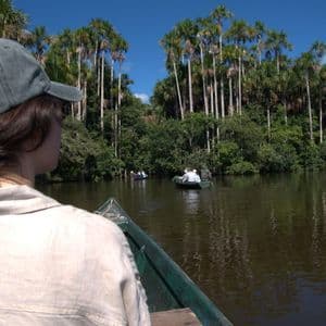Eine WeRoad-Gruppenreise führt mit kleinen Booten auf einem ruhigen Fluss entlang, der von dichtem Dschungel mit hohen Palmen umgeben ist.