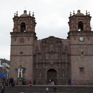 Eine große, reich verzierte Steinkirche mit zwei Glockentürmen steht auf einem öffentlichen Platz mit Menschen auf ihren Stufen.