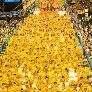 An elevated view of a nighttime parade with a large group of performers in elaborate yellow costumes and headdresses.