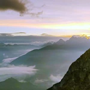 Una vista panoramica di una catena montuosa con cime che emergono dalle nuvole sotto un cielo all'alba.