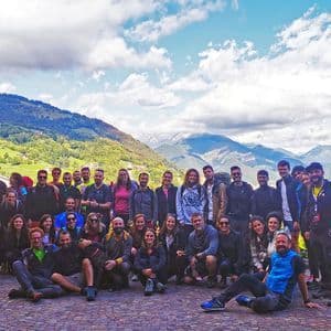 Un gruppo WeRoad in viaggio posa per una foto su una piazza di ciottoli che si affaccia su una lussureggiante valle montuosa verde sotto un cielo parzialmente nuvoloso.