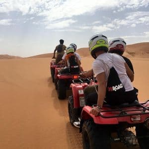 Un viaje en grupo de WeRoad en quads rojos en fila por las dunas del desierto bajo un cielo nublado.