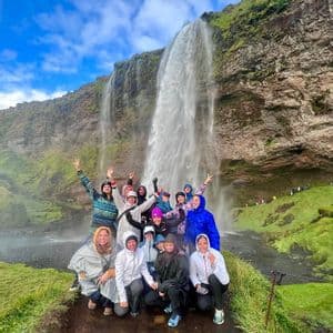 Un groupe WeRoad en imperméables sourit et pose pour une photo devant une grande cascade sur une falaise moussue.