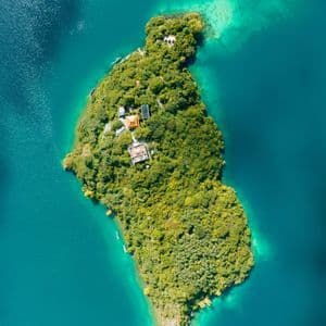 Una veduta aerea dall'alto di un'isola verde e lussureggiante con edifici immersi tra gli alberi, circondata da vivaci acque turchesi.