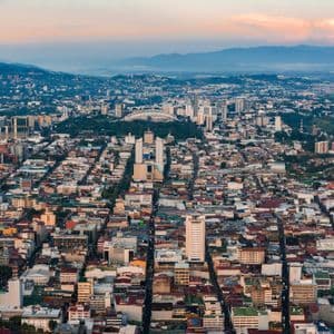 Una vista aérea de un denso paisaje urbano al amanecer, con calles y edificios que conducen hacia las montañas en el horizonte.