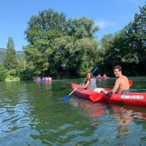 Un hombre y una mujer de un viaje en grupo de WeRoad en una canoa roja en un río, con otros kayakistas y una orilla boscosa al fondo.