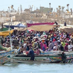 Un marché animé au bord de l'eau avec une foule nombreuse et des bateaux de pêche colorés amarrés le long du rivage.
