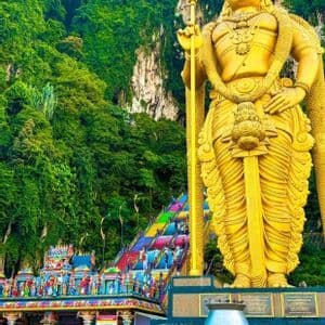 Una grande statua dorata di una divinità sorge accanto a una scalinata color arcobaleno che ascende una ripida scogliera boscosa.