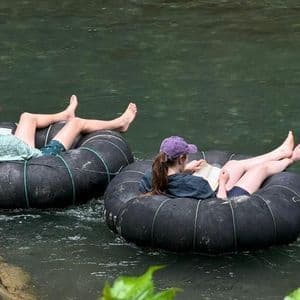 Due persone di un viaggio di gruppo WeRoad leggono libri mentre si rilassano su ciambelle in un fiume.