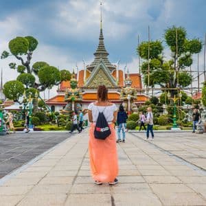 Una mujer de espaldas con una mochila WeRoad mira un templo grande y ornamentado flanqueado por dos estatuas gigantes en un patio.