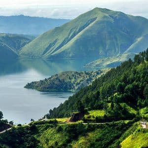 Una vista panoramica su una strada tortuosa mostra un grande lago circondato da rigogliose montagne verdi e foreste.