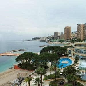 Una vista dall'alto di una città costiera con una spiaggia sabbiosa, una grande piscina e edifici moderni sotto un cielo coperto.
